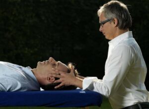Ein Mann erhält bei einem Osteopathen in Hamburg eine entspannende Kopfmassage von einem anderen Mann.