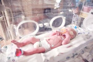 Ein Baby liegt mit einem Schnuller in einem Brutkasten und wird von einem erfahrenen Osteopathen in Hamburg betreut.