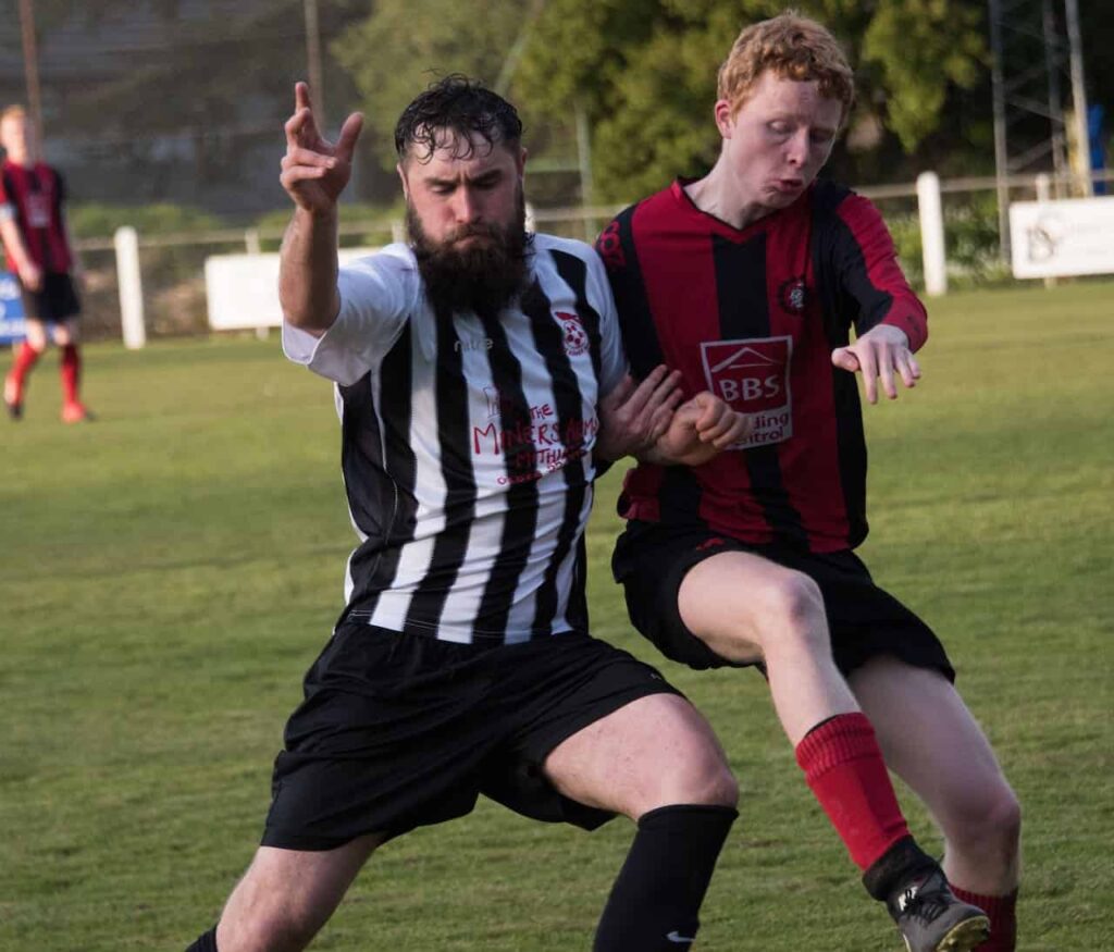 Zwei Männer spielen Fußball auf einem Feld und werden in Hamburg osteopathisch behandelt.