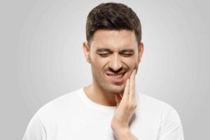 Ein Mann, der unter Zahnschmerzen leidet, hält schmerzerfüllt seine Hand und sucht Linderung durch osteopathische Techniken.