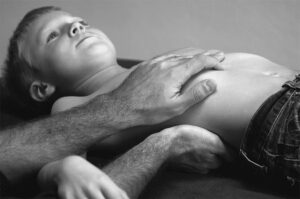 Ein Schwarz-Weiß-Foto eines kleinen Jungen, der auf dem Bauch liegt und sich einer osteopathischen Behandlung unterzieht.