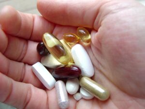 Die Hand einer Person hält eine Vielzahl von Vitaminen und Nahrungsergänzungsmitteln und betont die Bedeutung der Kinderosteopathie.