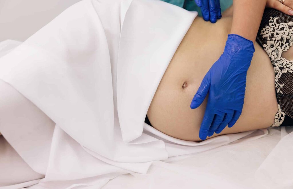 Eine schwangere Frau, die in Hamburg Kinderosteopathie erhält, liegt mit blauen Handschuhen bequem auf einem Bett.