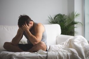 Ein Mann sitzt mit nachdenklichem Gesichtsausdruck auf einem Bett und denkt über Osteopathie Hamburg nach.
