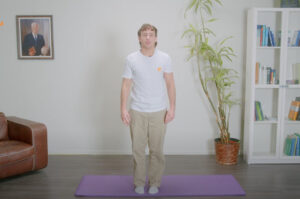 Ein Mann übt Zittern gegen Stress auf einer Yogamatte im Wohnzimmer.