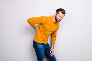 Mann im orangefarbenen Pullover leidet unter Rückenschmerzen und demonstriert Rückenschmerz-Resilienz.